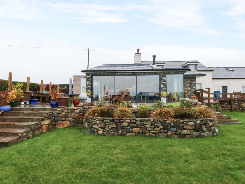 A garden with a stone wall and glass conservatory at Bryn Mor Cottage in Mynytho near Llanbedrog