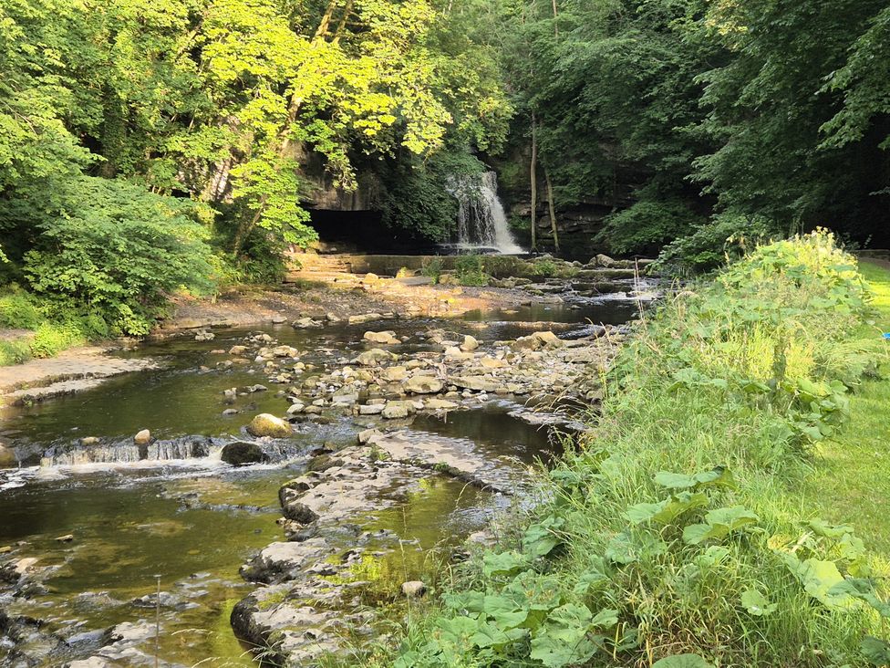 A river with rocks and a waterfall at Ivy Cottage in West Burton