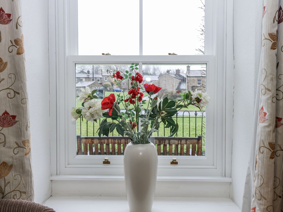 A living room with a window view and a vase of flowers at Ivy Cottage in West Burton
