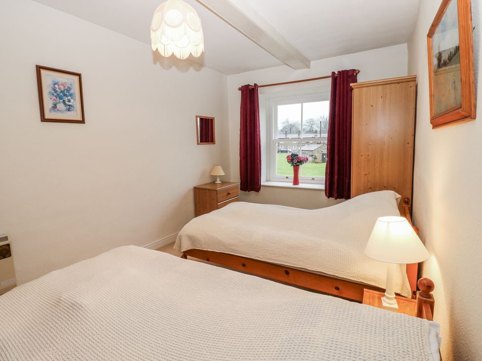 A bedroom with two beds and a window at Ivy Cottage in West Burton