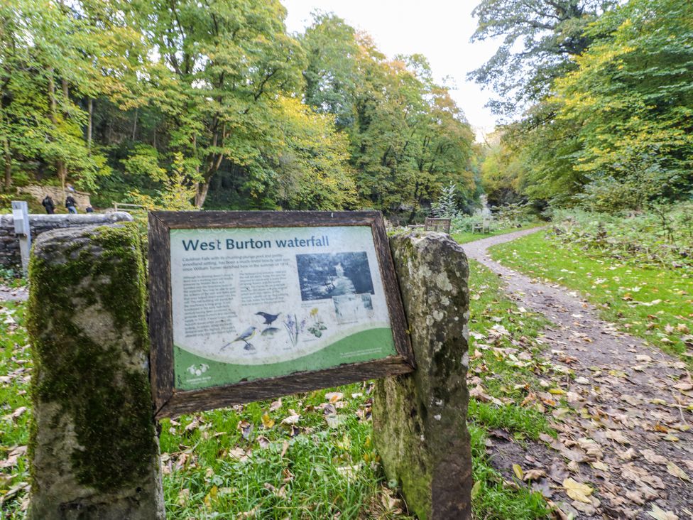 An information board about West Burton waterfall in a forested area at Ivy Cottage West Burton