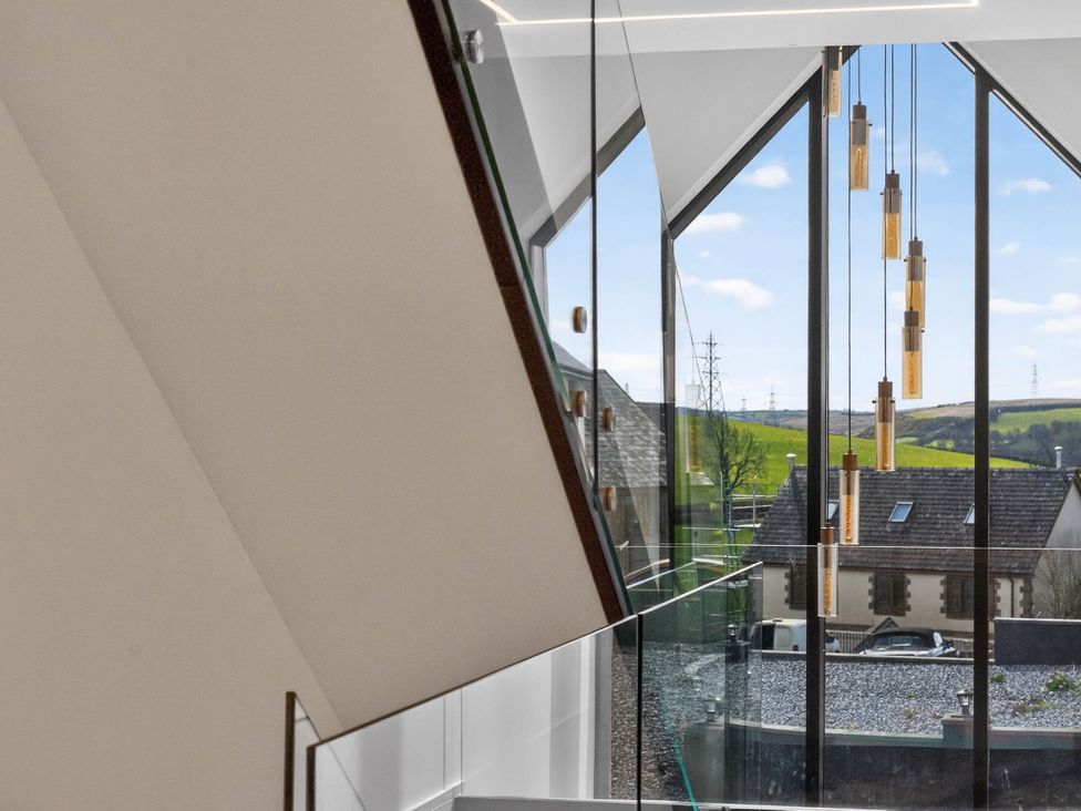 A staircase with glass railing and hanging light fixtures at Heddfan in Carmarthen