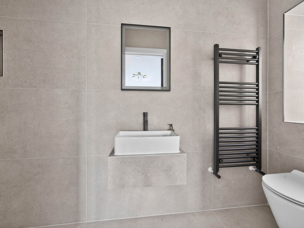 A bathroom with a sink, toilet, mirror, and towel radiator at Ty Uchel