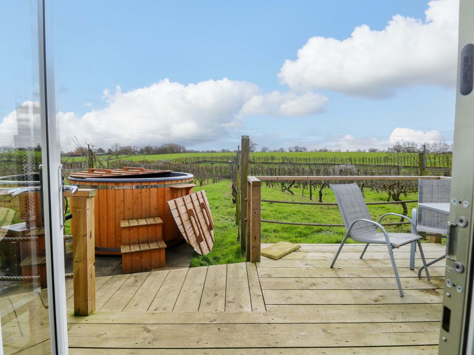 An outdoor area with a hot tub and chairs near a vineyard at Grape Escape near Halesworth