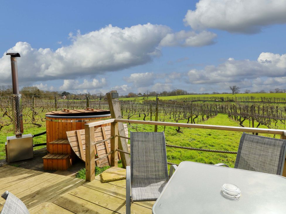 An outdoor seating area with a hot tub and vineyard view at Grape Escape near Halesworth
