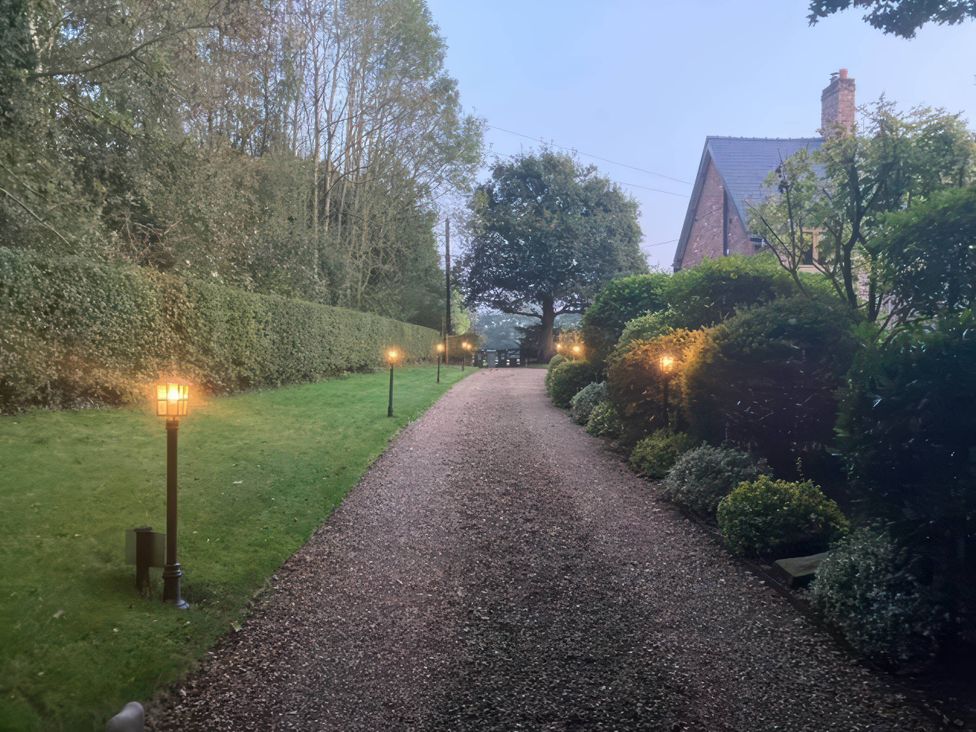 A pathway lined with lamps and hedges leading to a house at Acorn Cottage in Knutsford