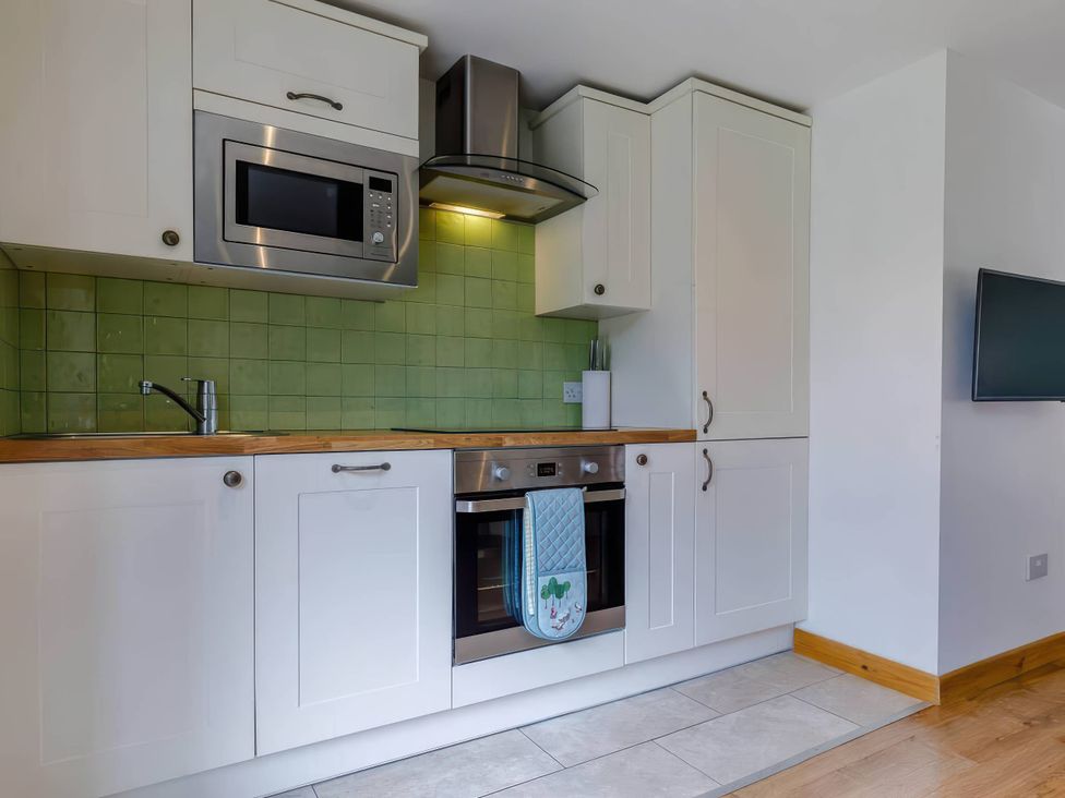 A kitchen with a microwave, oven, and sink at Acorn Cottage in Knutsford
