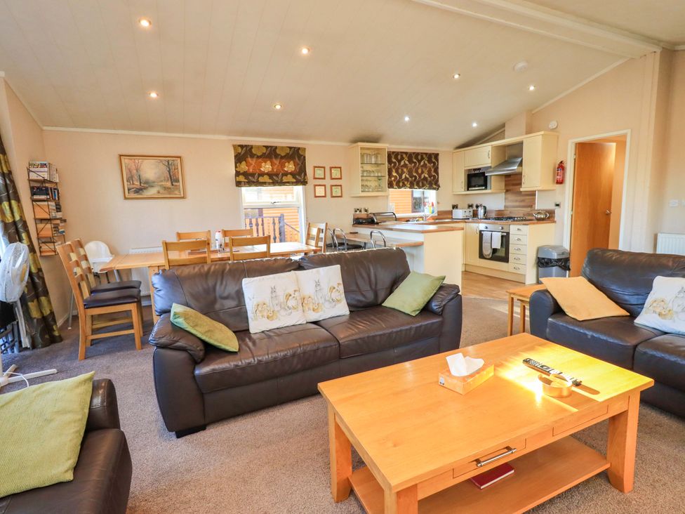 A living room with a sofa, coffee table, and dining area at Kingfisher Lodge