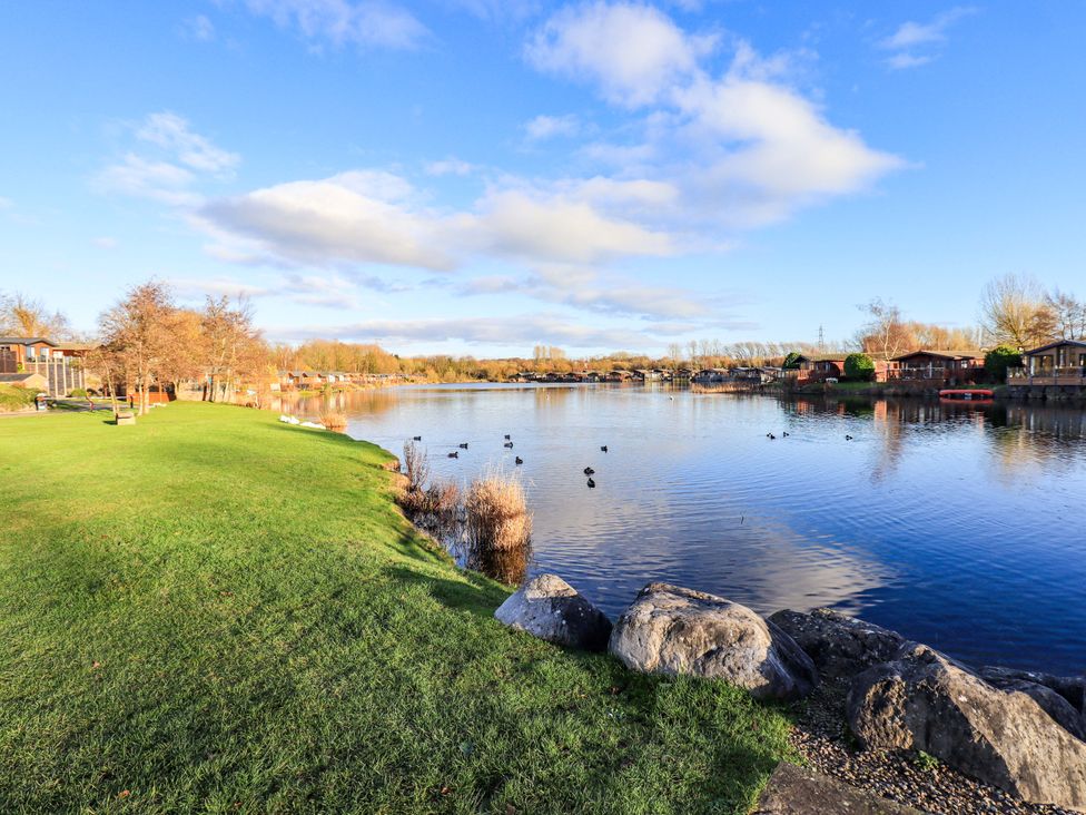 A lakeside view with grass and trees at Kingfisher Lodge