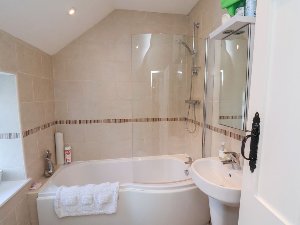 A bathroom with a bathtub, shower, and sink at Cheyne Cottage in Fylingthorpe