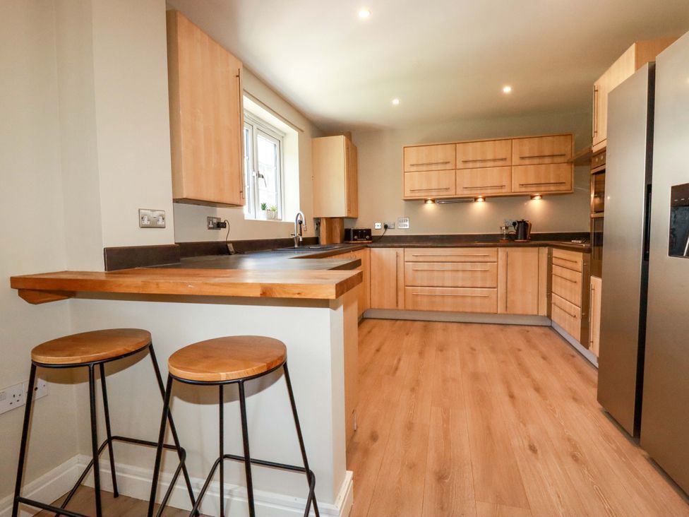 A kitchen with wooden cabinets and bar stools at 3 Rope Walk in St. Austell