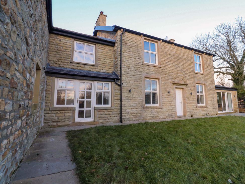 An exterior view of a stone house with grass in front at The Farm House in Skipton
