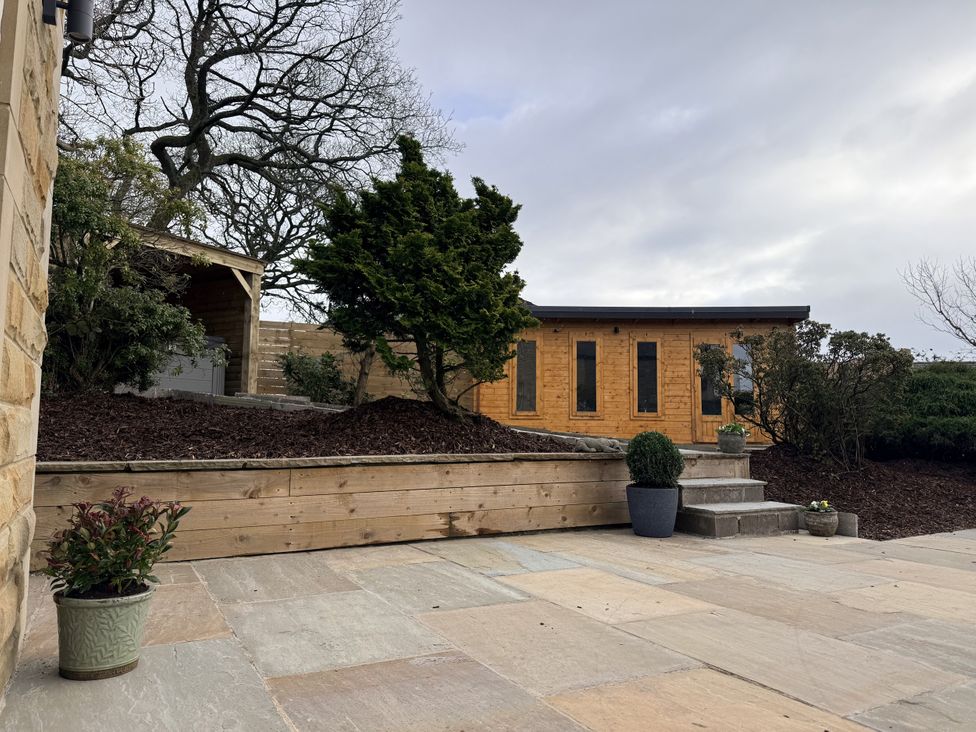 A garden with a wooden cabin and stone patio at The Farm House in Wigglesworth near Settle