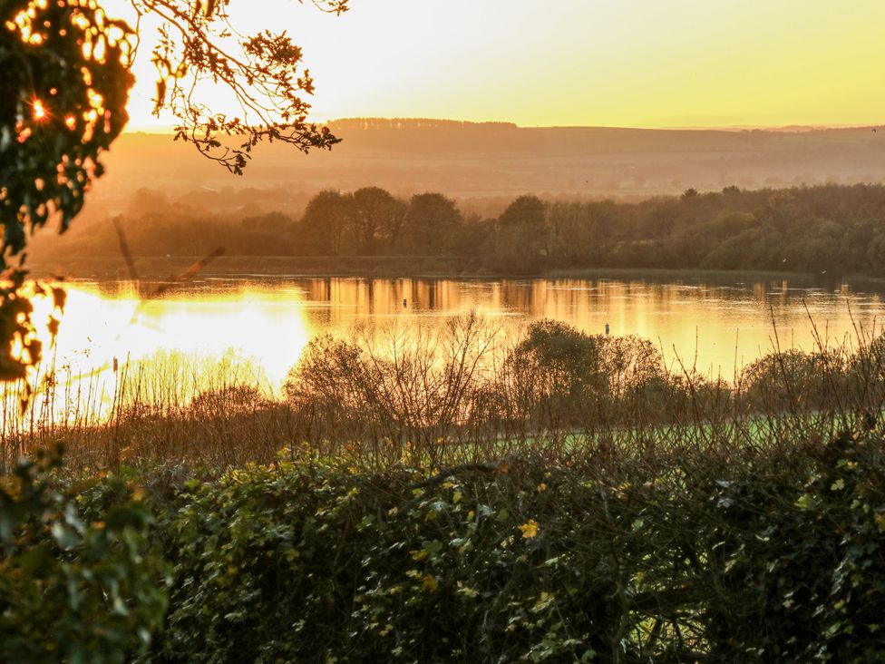 A view of a sunset over a lake surrounded by trees and bushes at The Robins Nest in 