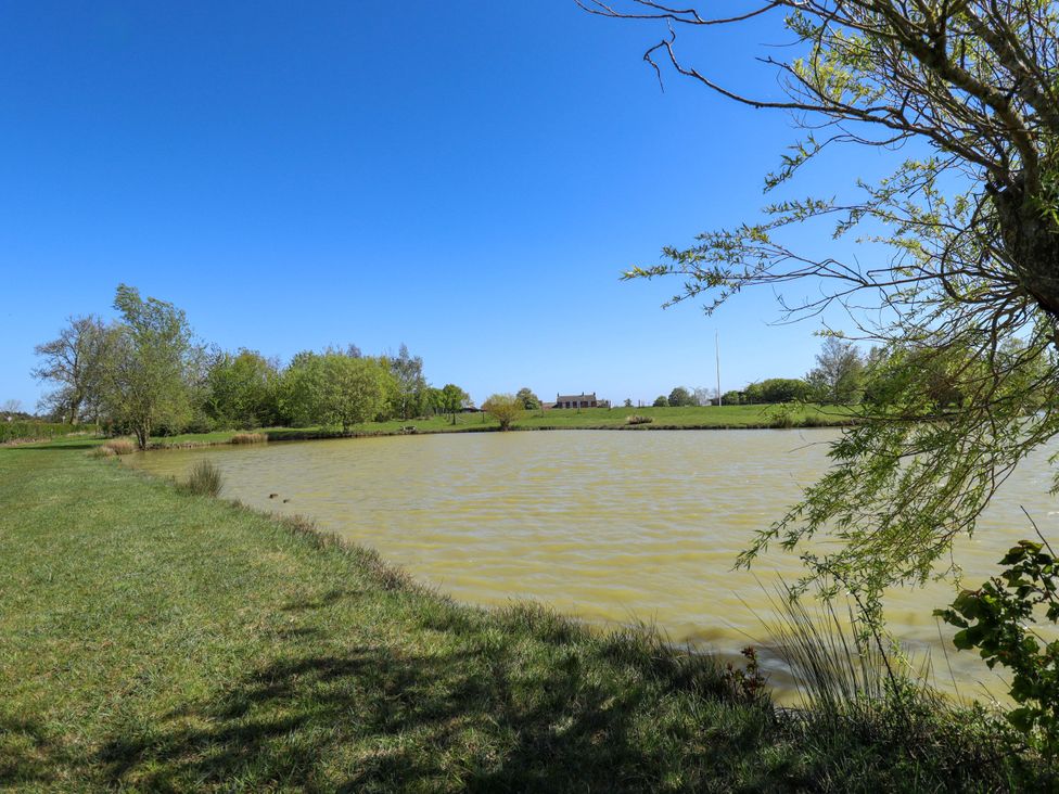 A pond with trees and a building in the background at Barn Owl near Louth
