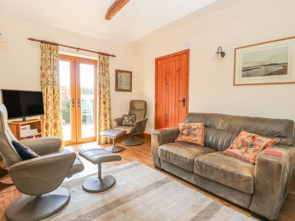 A living room with a sofa, armchair, and television at Kingfisher in Louth