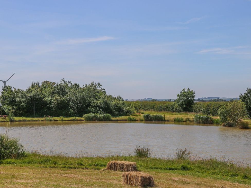 A pond surrounded by grass and trees at Kingfisher in Louth