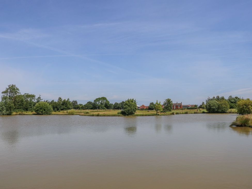 A view of a pond surrounded by trees and fields at Kingfisher in Louth