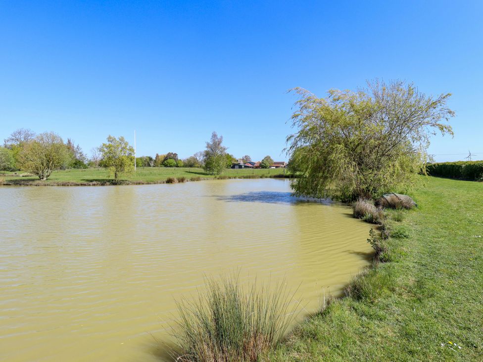 A pond surrounded by grass and trees at Kingfisher near Louth