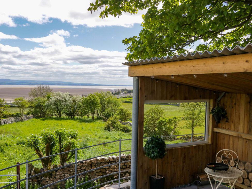 An outdoor area with a table and chair overlooking greenery at Little Hut in Grange-Over-Sands