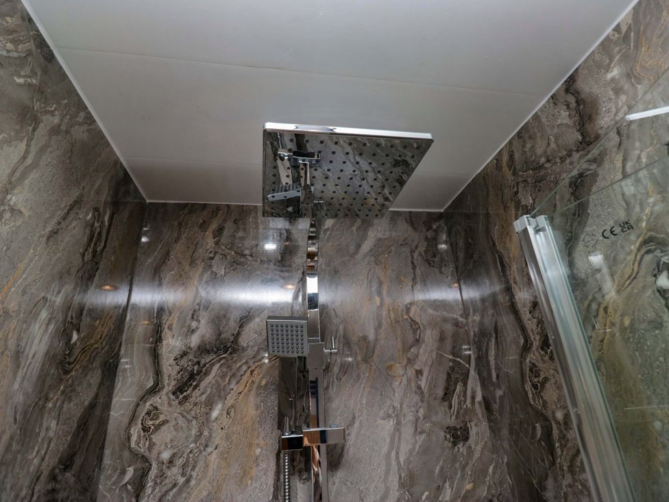 A shower with a rain shower head and marble walls at Little Hut in Grange-Over-Sands
