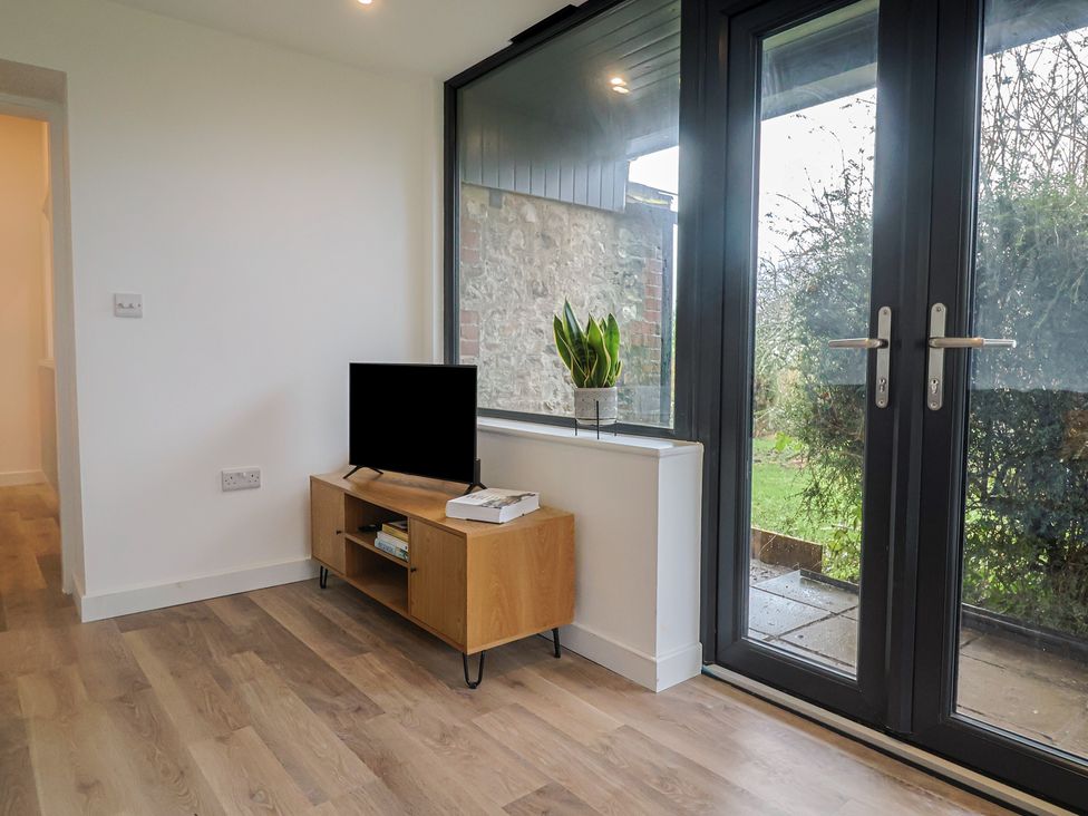 A living room with a television and sliding doors at Little Poppes Lawn in Holditch near Hawkchurch