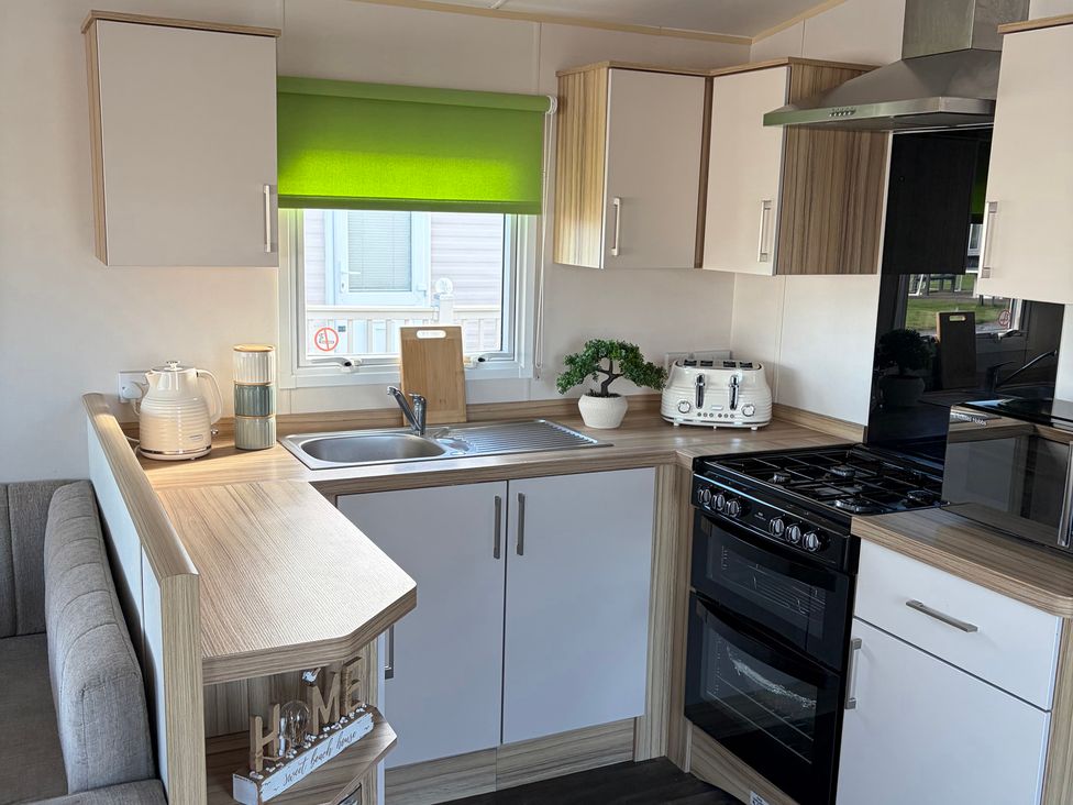 A kitchen with cabinets, sink, stove, and appliances at The Beachside Hideout - St Michaels Caravan Park, Towyn