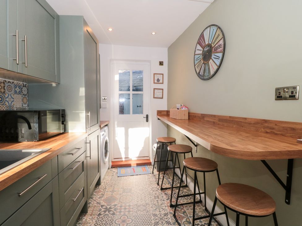 A kitchen with cabinets, a microwave, and bar stools at The Corner Cottage in Gloucester