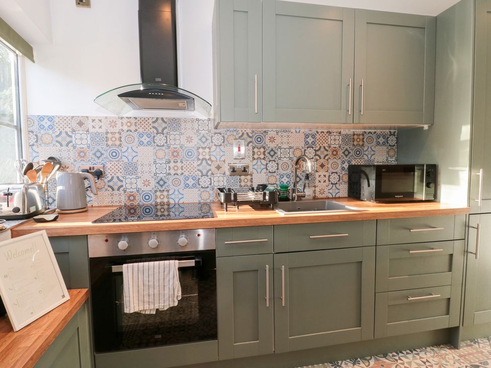 A kitchen with cabinets, a sink, a cooker, and a microwave at The Corner Cottage in Gloucester