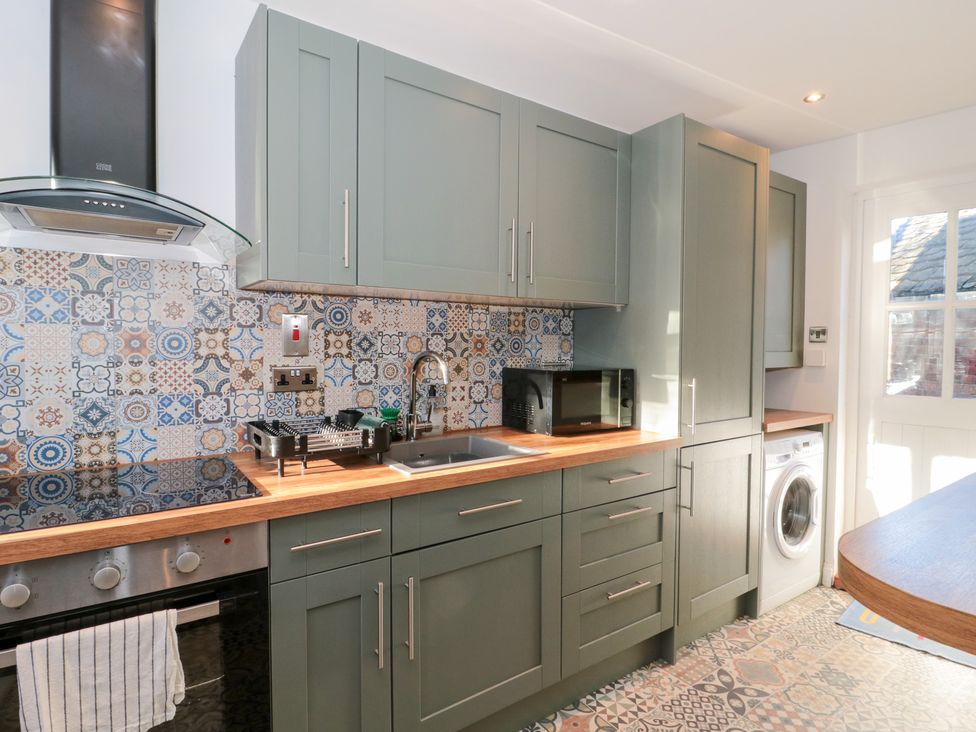 A kitchen with cabinets, sink, stove, microwave, and washing machine at The Corner Cottage in Gloucester
