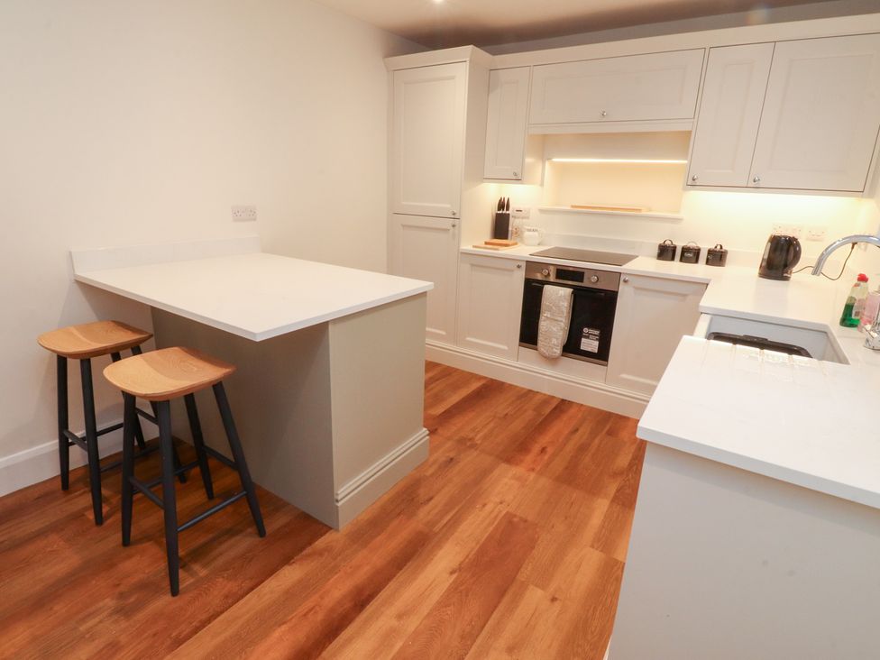 A kitchen with a countertop, bar stools, and appliances at Cobble Cottage Clitheroe