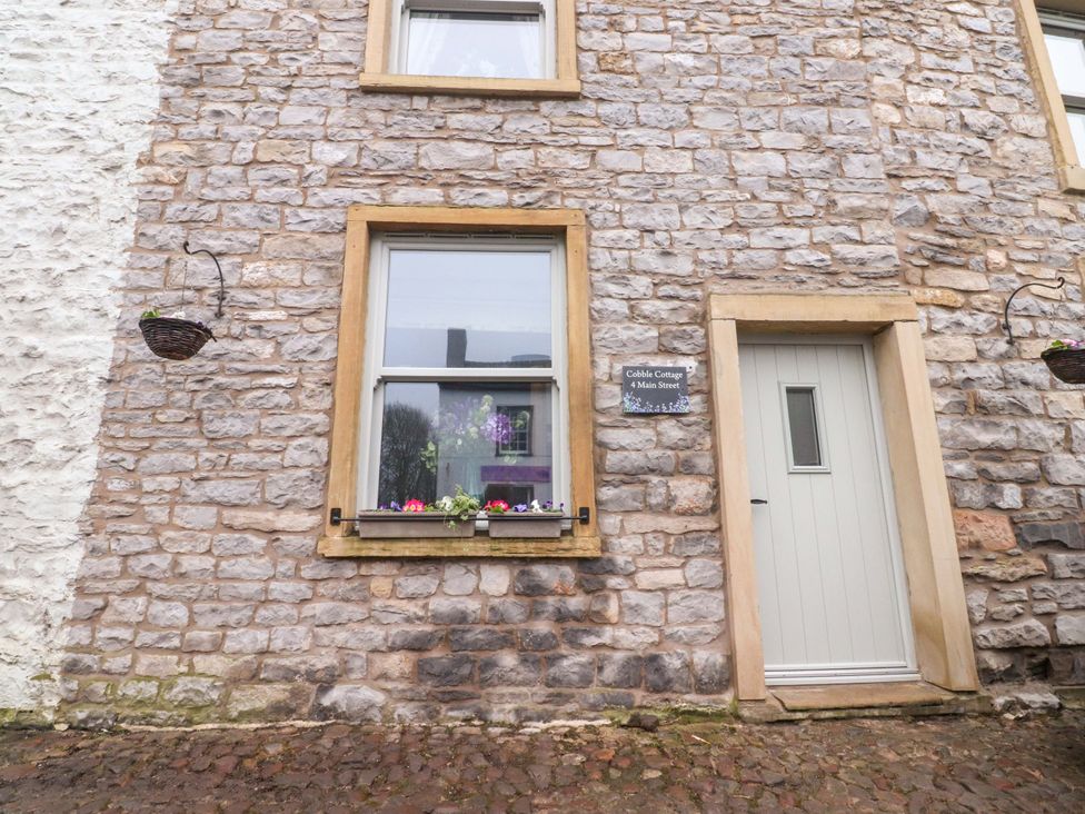 An outdoor view of a stone cottage with a door and flower box at Cobble Cottage in Gisburn