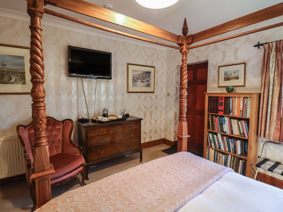 A bedroom with a bed, armchair, dresser, and bookshelf at The Gun Room in Beccles