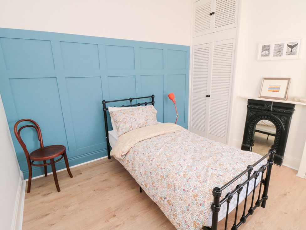 A bedroom with a bed, chair, and shelving at Cattersty Cottage