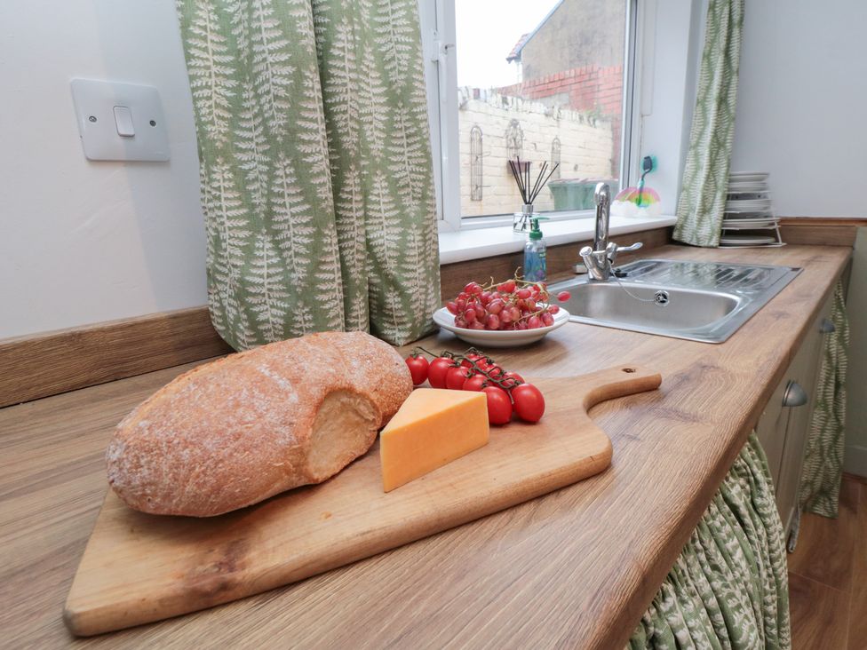 A kitchen counter with bread, cheese, tomatoes, and grapes at Cattersty Cottage in 