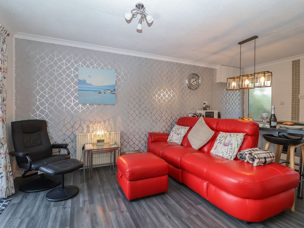 A living room with a red sofa and kitchen area at Westview in Liskeard