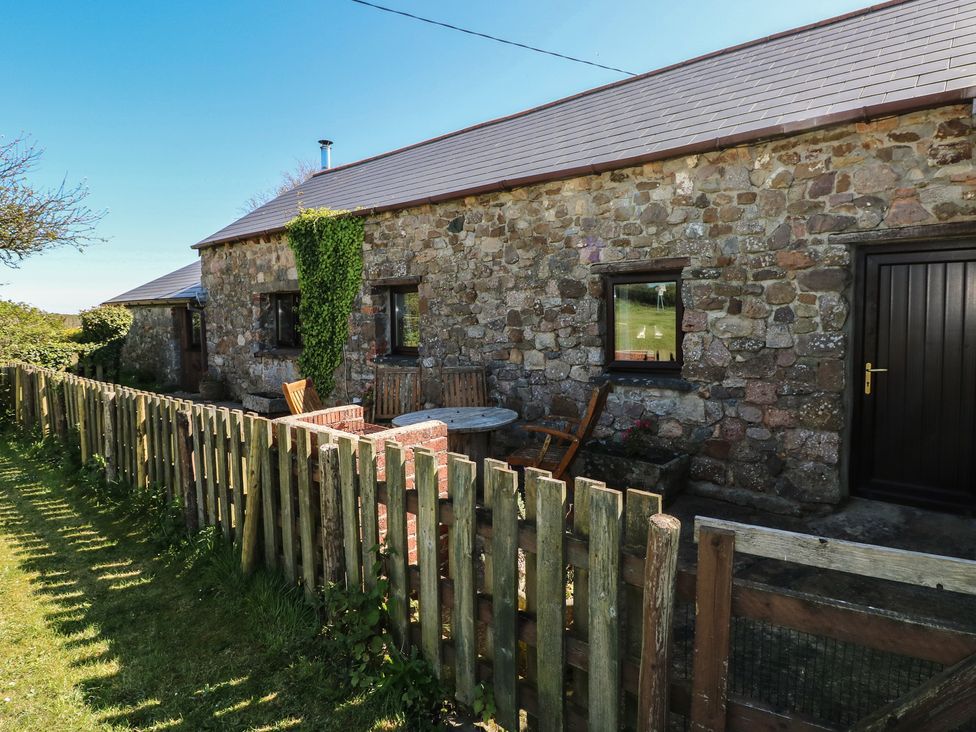 An outdoor area with a stone wall and wooden table at Butterslade in Port Eynon