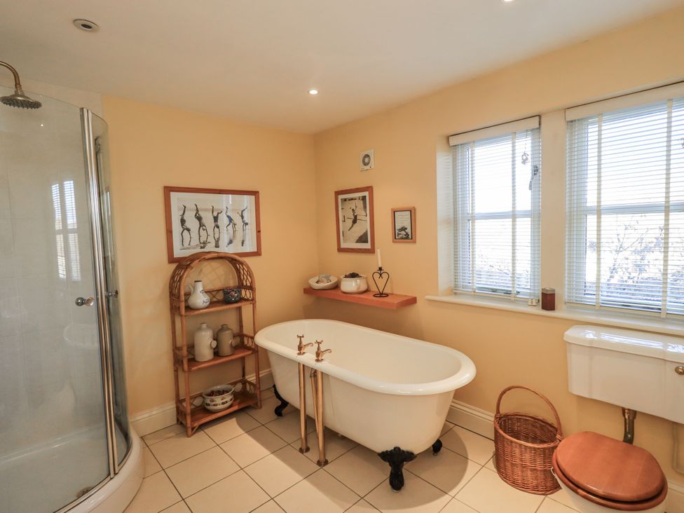 A bathroom with a bathtub, shower, and shelf at Orchard House in Leyburn