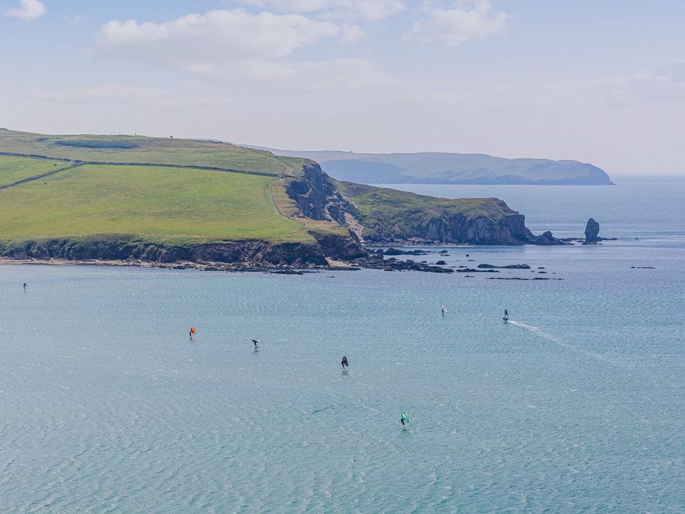A coastal scene with surfers on water and a hill in the background at 6 Avon Quillet Bigbury-On-Sea