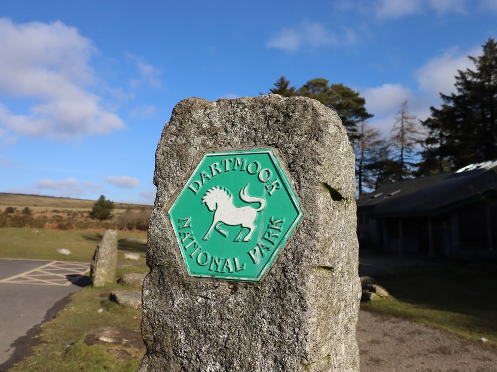 A sign for Dartmoor National Park near stone and trees at Swallows Nest in Widecombe-in-the-Moor near Postbridge