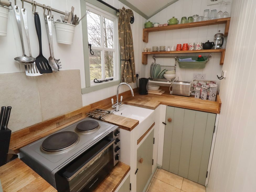 A kitchen with a sink, stove, and shelves at Woodland in Hexham
