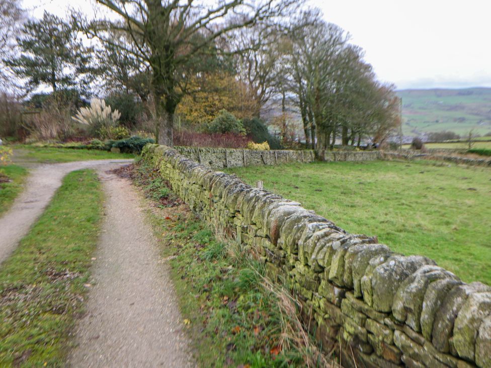 A pathway and stone wall surrounded by grass and trees at The Farmhouse in High Peak