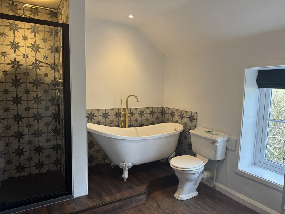 A bathroom with a bathtub, shower, toilet, and window at The Farmhouse in High Peak