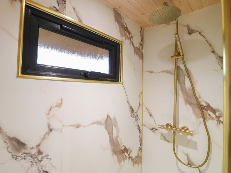 A shower with gold fixtures and a window at The Sty in Derby