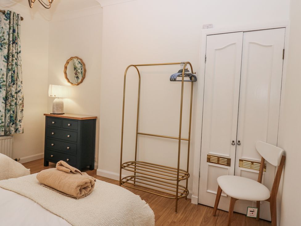 A bedroom with a bed, dresser, lamp, and clothes rack at Cairndhu, Bossiney