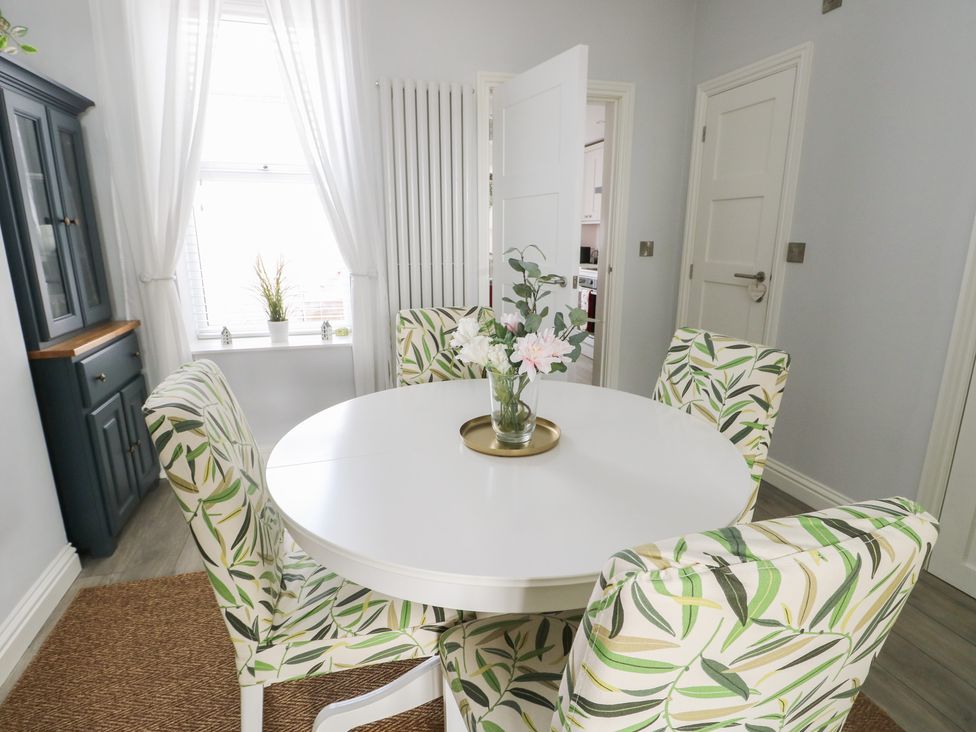 A dining room with a round table and floral chairs at Bryn Y Mor Beaumaris
