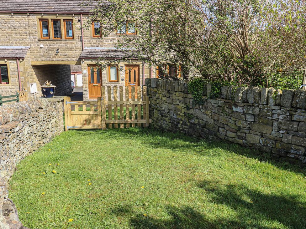 A garden with a stone wall and wooden gate at Moorview in Holmfirth