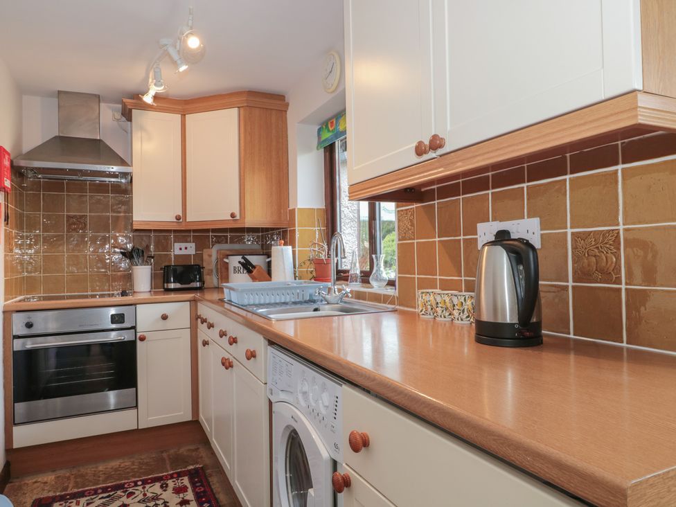 A kitchen with cabinets, sink, kettle, and washing machine at The Cowshed in Bristol