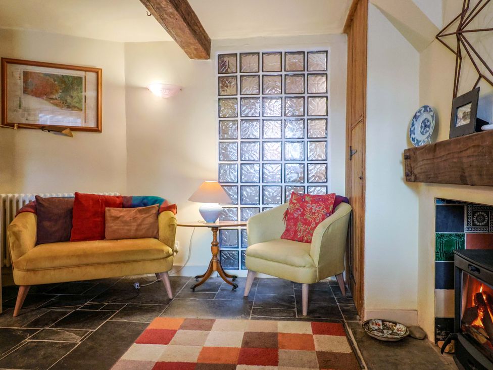A living room with a yellow sofa, green armchair, and fireplace at Rope Cottage in Bridport