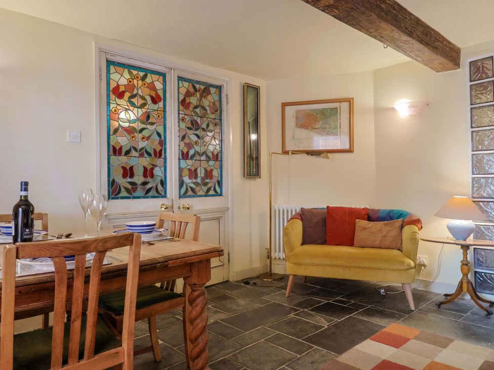 A living room with a dining table and stained glass windows at Rope Cottage in Bridport